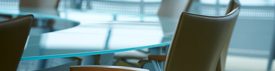Images of a boardroom that features empty tan chairs and a clear glass table.